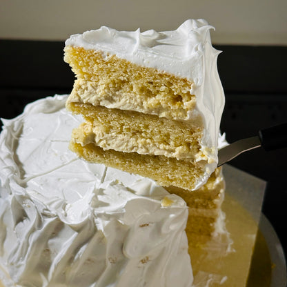 Slice of layered cake with white frosting on a fork, with the rest of the cake in the background.